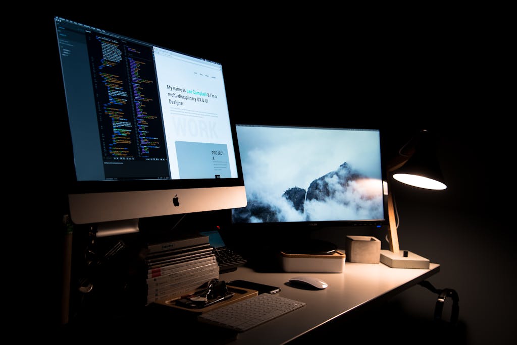 A clean and stylish workspace featuring dual monitors, a lamp, and office supplies.